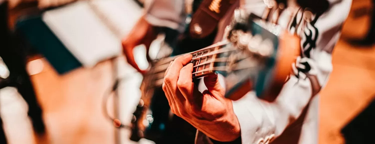 Close-up of a musician playing a bass guitar with a blurred background, warm tones.